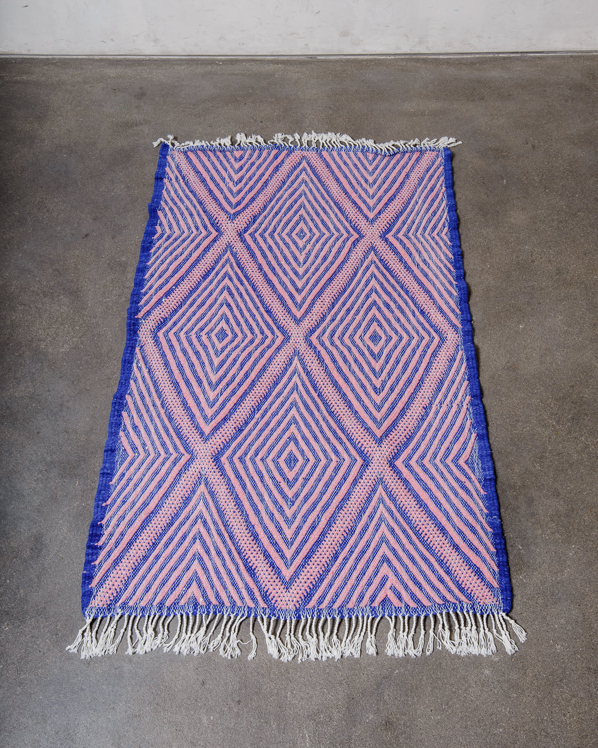 Small Berberlin Kelim Rug in pink and blue laying on concrete floor.